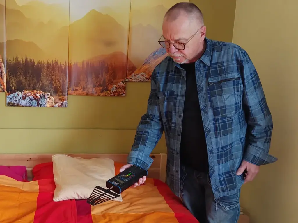 Ein Untersucher hält ein elektronisches Messgerät mit Antenne über ein Doppelbett.